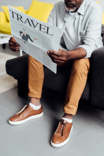 african american man sitting on sofa and reading travel newspaper  - Photo, Image