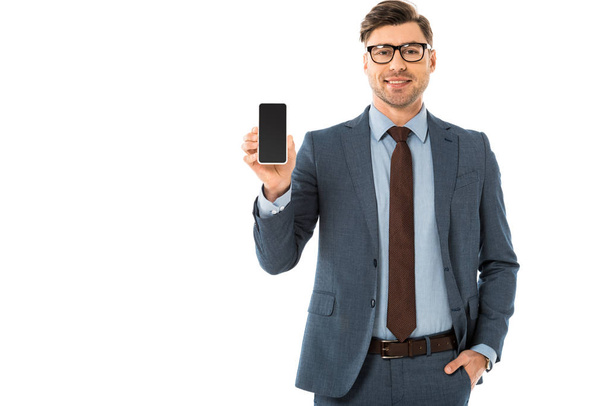 handsome businessman in suit showing blank screen on smartphone isolated on white - Foto, Imagem