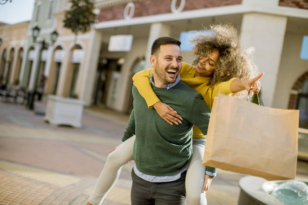 Portret van jonge man houdt jonge vrouw op zijn rug, veel plezier en gaan om te winkelen - Foto, afbeelding