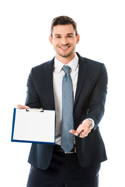smiling businessman in suit showing empty clipboard and pen isolated on white  - Φωτογραφία, εικόνα