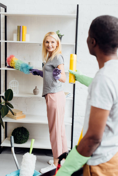 blonde smiling woman with duster in hand taking yellow spray  - Fotoğraf, Görsel