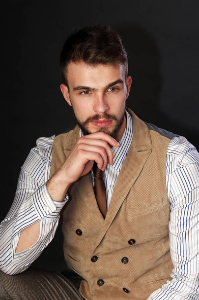 closeup portrait of the beautiful charismatic young man with a beard wearing pants, shirt, vest and tie on a dark background studio - Foto, afbeelding