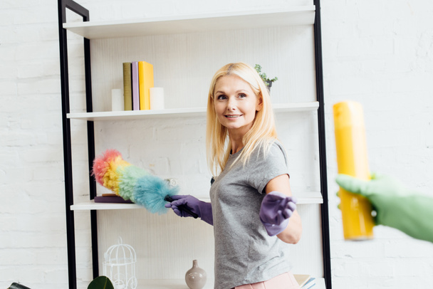 blonde smiling woman with duster in hand taking yellow spray  - Фото, изображение