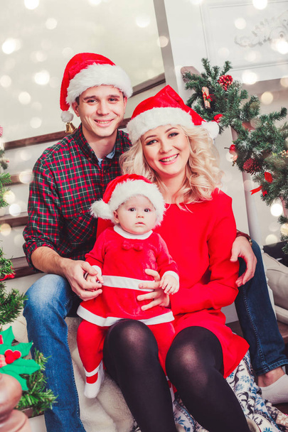 Рождественская семья улыбается у елки. Гостиная украшена елкой и подарочной коробкой, свет придает уютную атмосферу. Новогодняя тема. Тонирование
 - Фото, изображение