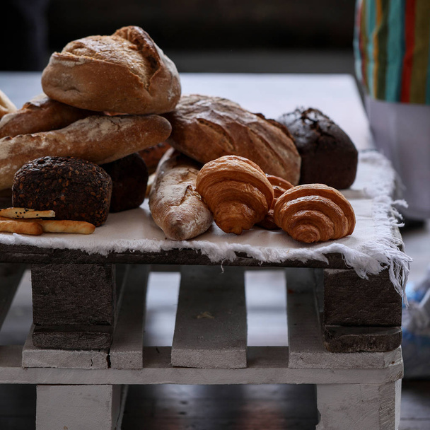 Different kind of bread at white napkin on wooden pallet. Brown grain bread, croissant, baguette, loaf and other - Foto, imagen