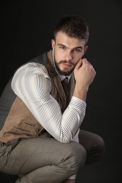 closeup portrait of the beautiful charismatic young man with a beard wearing pants, shirt, vest and tie on a dark background studio - Fotó, kép