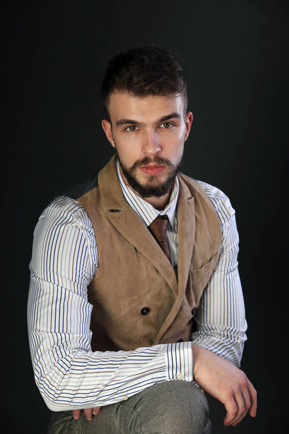 Portret van de close-up van de mooie charismatische jonge man met een baard dragen broek, shirt, vest en stropdas op een donkere achtergrond studio - Foto, afbeelding