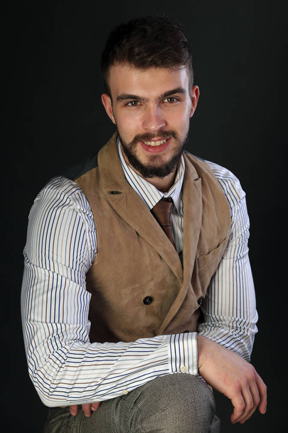 Detailní portrét krásné charismatický mladý muž s vousy nosit kalhoty, košile, vesta a kravata na tmavém pozadí studio - Fotografie, Obrázek