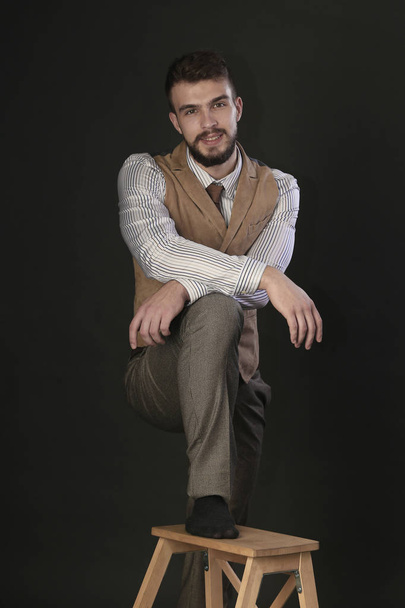 closeup portrait of the beautiful charismatic young man with a beard wearing pants, shirt, vest and tie on a dark background studio - Fotografie, Obrázek