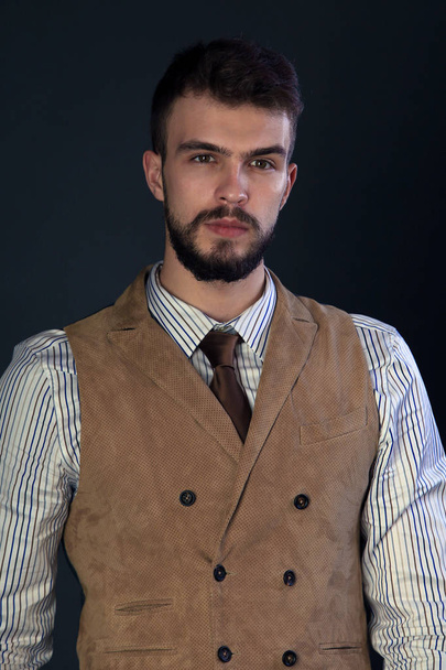 closeup portrait of the beautiful charismatic young man with a beard wearing pants, shirt, vest and tie on a dark background studio - Foto, Imagem