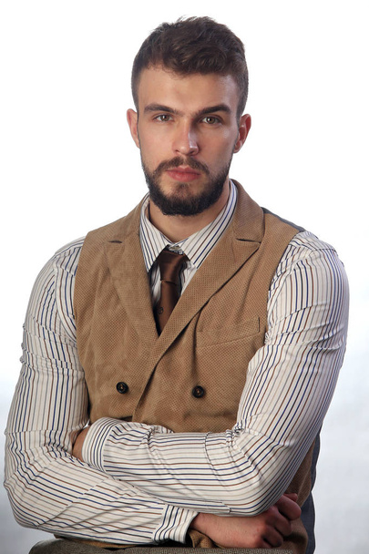 retrato de cerca del hermoso joven carismático con una barba usando pantalones, camisa, chaleco y corbata en un estudio de fondo oscuro
 - Foto, Imagen