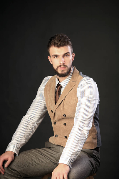 closeup portrait of the beautiful charismatic young man with a beard wearing pants, shirt, vest and tie on a dark background studio - Foto, immagini