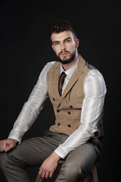 closeup portrait of the beautiful charismatic young man with a beard wearing pants, shirt, vest and tie on a dark background studio - Foto, Imagen