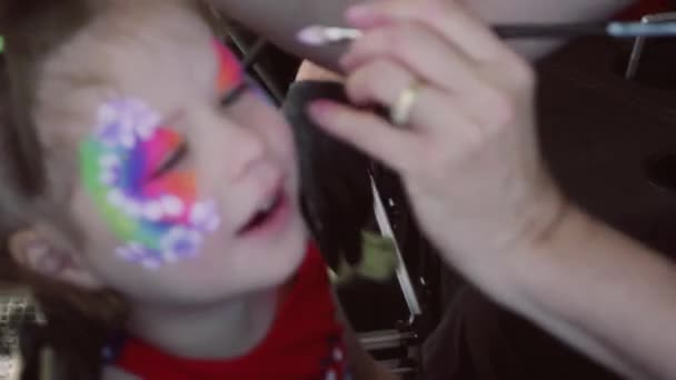Pieni tyttö maalauttaa kasvonsa karnevaalissa.
 - Materiaali, video