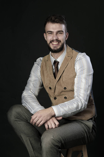 closeup portrait of the beautiful charismatic young man with a beard wearing pants, shirt, vest and tie on a dark background studio  - Foto, afbeelding