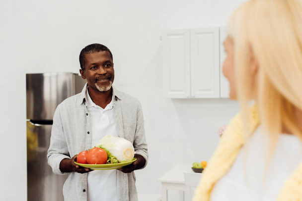 african american man holding vegetables and looking at woman  - Fotografie, Obrázek