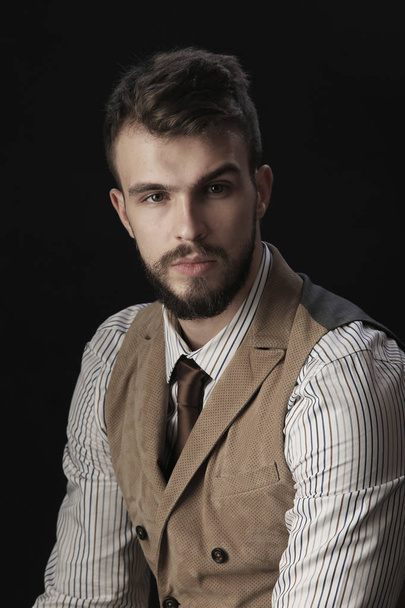 closeup portrait of the beautiful charismatic young man with a beard wearing pants, shirt, vest and tie on a dark background studio - Фото, зображення