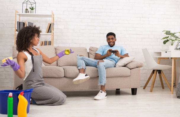 Frau putzt zu Hause, während ihr Freund auf der Couch ruht - Foto, Bild