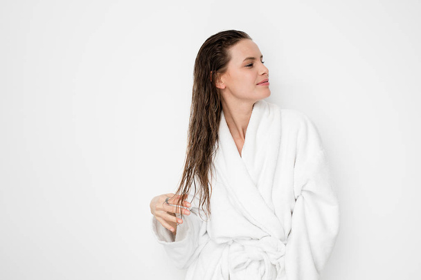 young natural and beauty woman standing with wet hair after a shower or a hair treatment in bathrobe on white background - Фото, изображение
