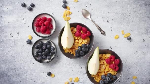 Flocons de maïs dorés aux fruits frais de framboises, bleuets et poires dans un bol en céramique - Séquence, vidéo