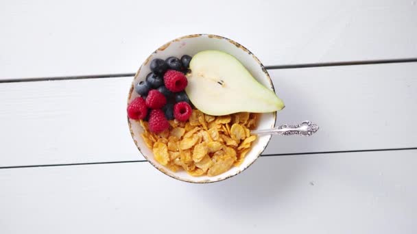 Golden cornflakes with fresh fruits of raspberries, blueberries and pear in ceramic bowl - Footage, Video
