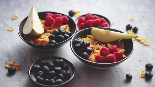 Copos de maíz dorados con frutas frescas de frambuesas, arándanos y pera en tazón de cerámica - Metraje, vídeo