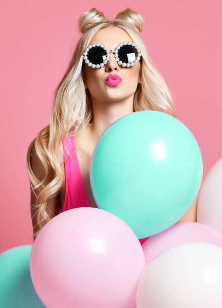 Trendy cheerful blonde woman on birthday party having fun with pastel color air balloons  blow kiss - Photo, Image