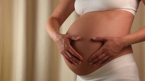 Close-up van zwangere Kaukasische vrouw holding en haar blootgestelde buik aanraken met hartvormige handen te anticiperen op de geboorte van de baby van profiel - Video