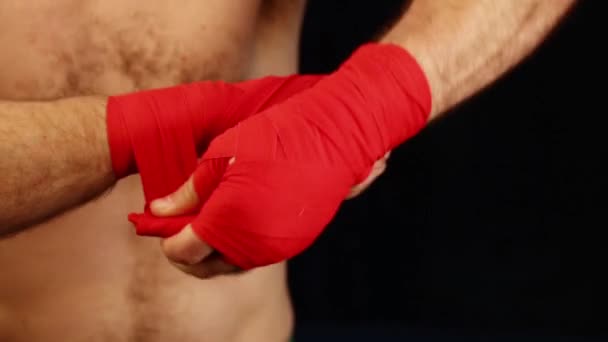 Cerca de hombre boxeador envolviendo envolturas de mano rojas sobre las muñecas preparándose para la lucha, sobre fondo negro con espacio de copia, vista de ángulo bajo - Imágenes, Vídeo