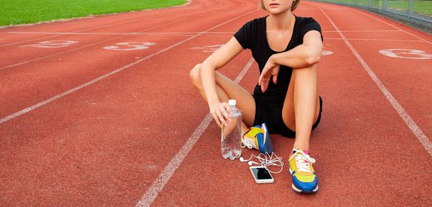 Woman runner in sportswear sitting on the running track of the stadium after training - Фото, зображення