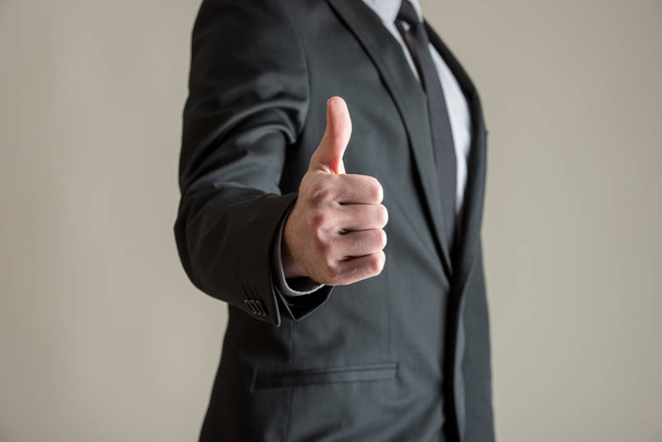 Вид спереди бизнесмена, показывающего большой палец вверх на сером фоне
. - Фото, изображение