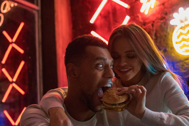 Young woman feeds a man a burger. Couple having fun. - Foto, Imagem