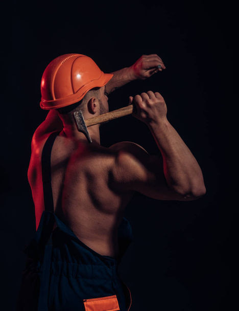It is under construction. Hard worker use muscular strength. Construction worker hammer a nail. Muscular man builder at work under construction. Man work with hammer - Foto, Imagen