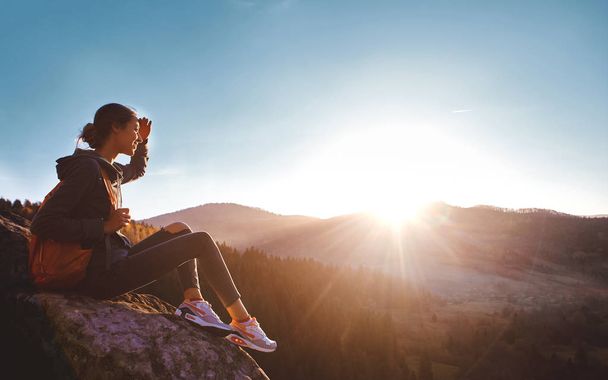woman sits on edge of cliff against background of sunrise - Foto, immagini