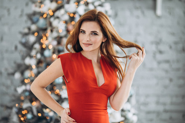 Christmas. Beautiful smiling woman Elegant over christmas tree in red dress lights background. happy new year. - Фото, зображення