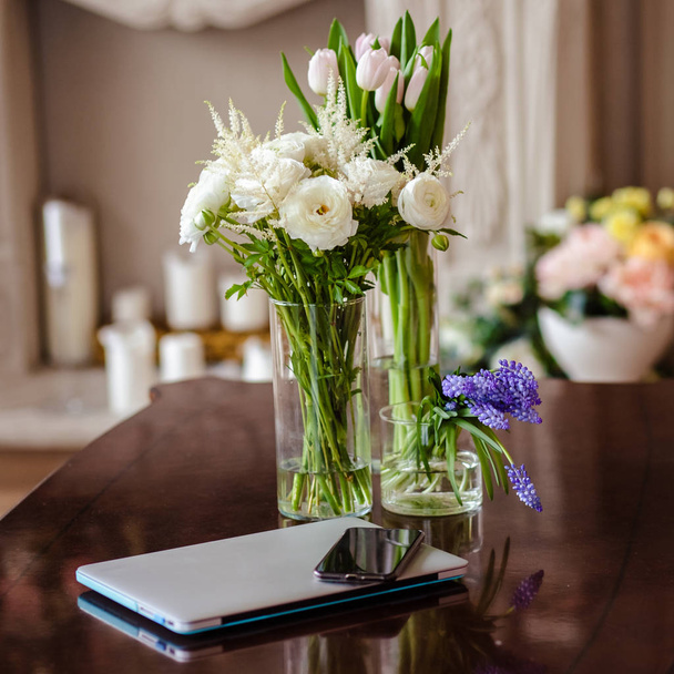 Bouquets of flowers in elegant simple vases on a table near mobile phone and laptop. Work place of florist decorator, lifestyle - Fotoğraf, Görsel