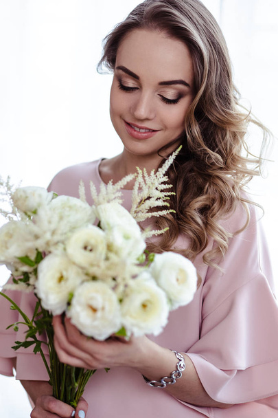 Beautiful young blonde woman with bouquet of white flowers. Portrait of pretty blonde girl in pink clothes. Florist in her work place - Фото, изображение