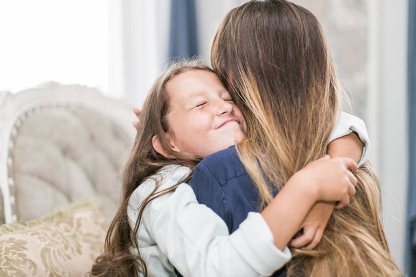 Beautiful young woman and her charming little daughter are hugging and smiling - Photo, image