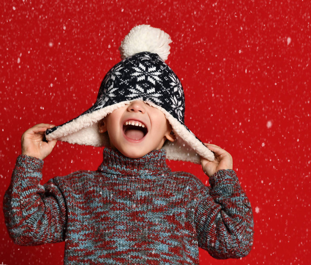 child boy in knitted hat and sweater and mittens having fun over colorful red  background. - Photo, image