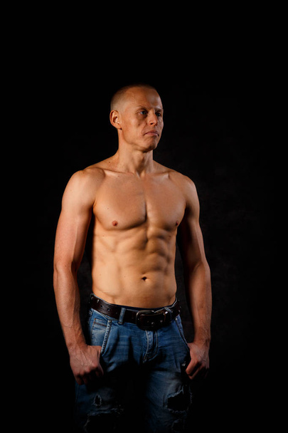 A muscular tattooed man on a dark background. - Zdjęcie, obraz