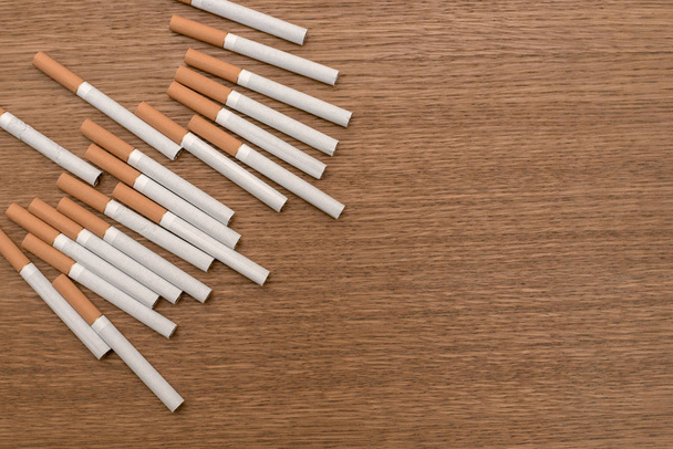A pack of white cigarettes with an orange filter on a wooden background on the edge of the surface. - Photo, Image