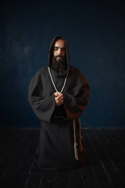 Monk in zwart gewaad met kap geknield en bidden, religie. Mysterieuze monnik in donkere Kaap - Foto, afbeelding