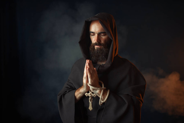 Средневековый монах в черном халате с капюшоном молится с закрытыми глазами, тайный ритуал. Загадочный монах в тёмном плаще. Тайна и духовность
 - Фото, изображение