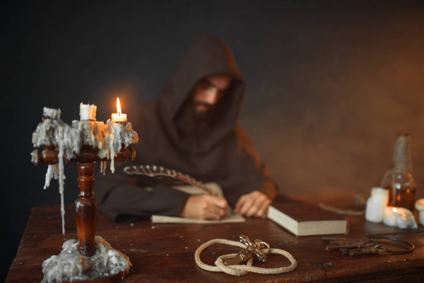 Middeleeuwse monnik zitten aan de tafel en schrijft met een gans veer, bovenaanzicht, geheime schrift. Mysterieuze monnik in donkere Kaap. Mysterie en spiritualiteit - Foto, afbeelding