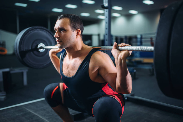 Gespierde powerlifter doen squats met barbell in sportschool. Training van Gewichtheffen, powerlifting opleiding in sportclub - Foto, afbeelding
