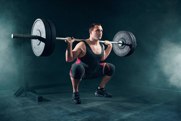 Powerlifter in sportswear doing squat with barbell in gym. Weightlifting workout, powerlifting training, lifter works with weight in sport club - Photo, Image