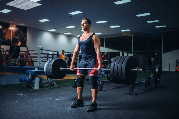Сильный мужчина-пауэрлифтер держит вес тяжелой штанги в спортзале. Тяжёлая атлетика, тренировка по поднятию тяжестей, спортсмен в спортивном клубе
 - Фото, изображение