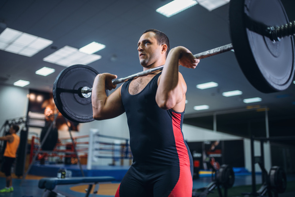 Сильный мужчина-пауэрлифтер поднимает штангу в спортзале. Тяжёлая атлетика, тренировка, спортсмен работает с весом в спортивном клубе
 - Фото, изображение