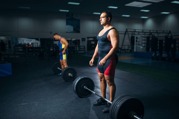 Two strong weightlifters doing exercise with barbells, gym interior on background. Weightlifting workout in fitness club, bodybuilding - Photo, Image