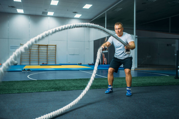 Мужчина спортсмен с веревками в спортзале, кроссфит тренировки. Кросс фитнес тренировки, силовые упражнения
 - Фото, изображение